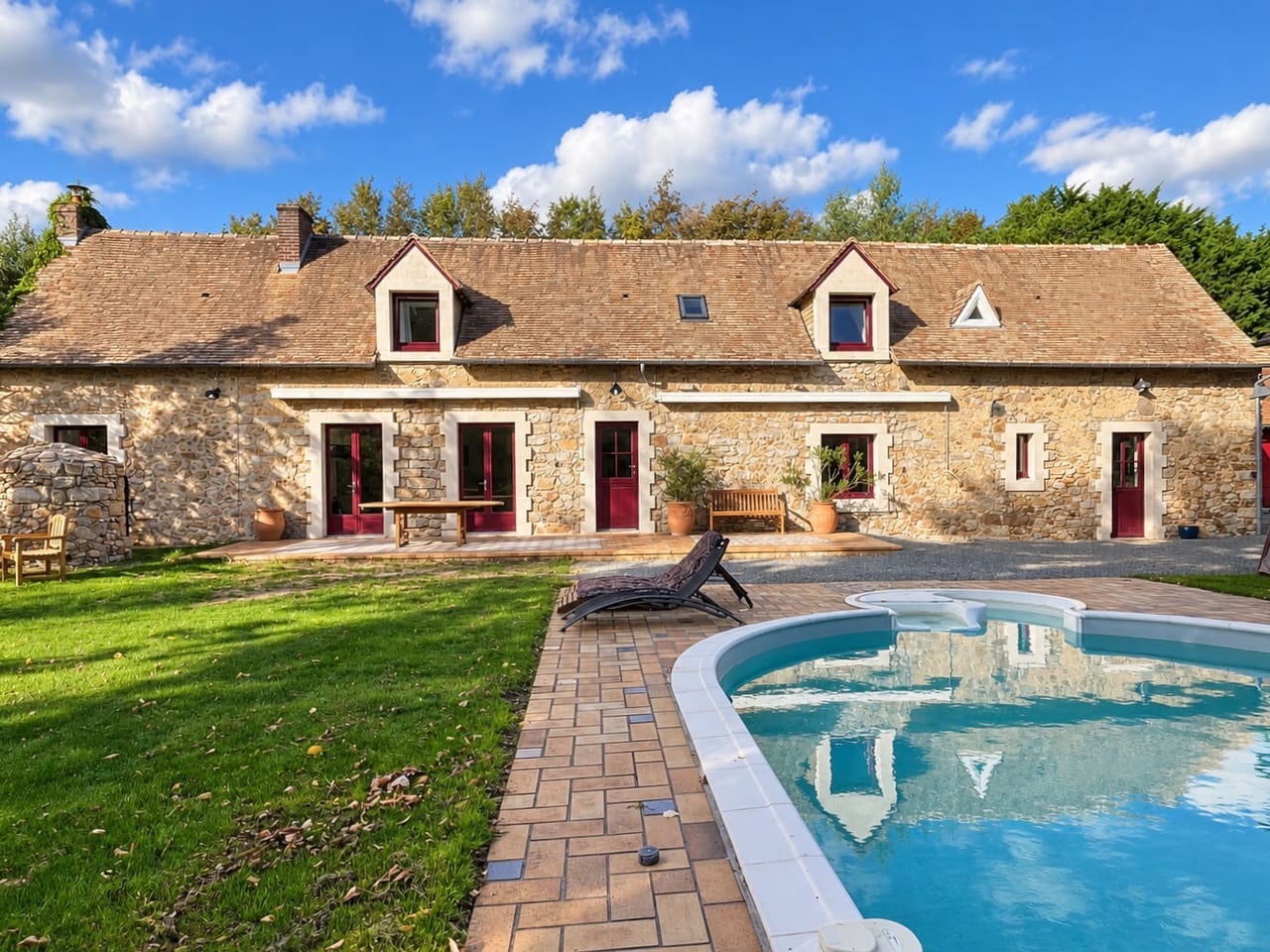 La ferme en pierre et sa piscine chauffée, vues depuis la pelouse du jardin