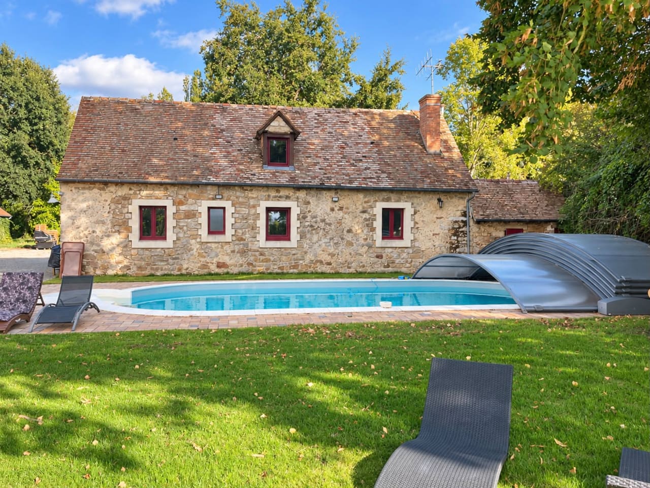 La piscine et son abri télescopique replié, transats posés sur la pelouse
